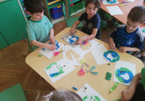 Trzech chłopców wykleja plasteliną w kolorze niebieskim i zielonym kulę ziemską.